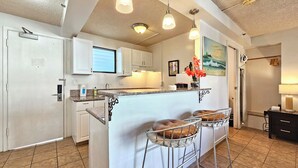 A kitchen with a central island, bar stools, a painting, and a ceiling light fixture. - Charming studio in wonderful Honolulu w/ WiFi & AC-Sleeps 3
WAIKIKI GRAND HOTEL® (Honolulu)