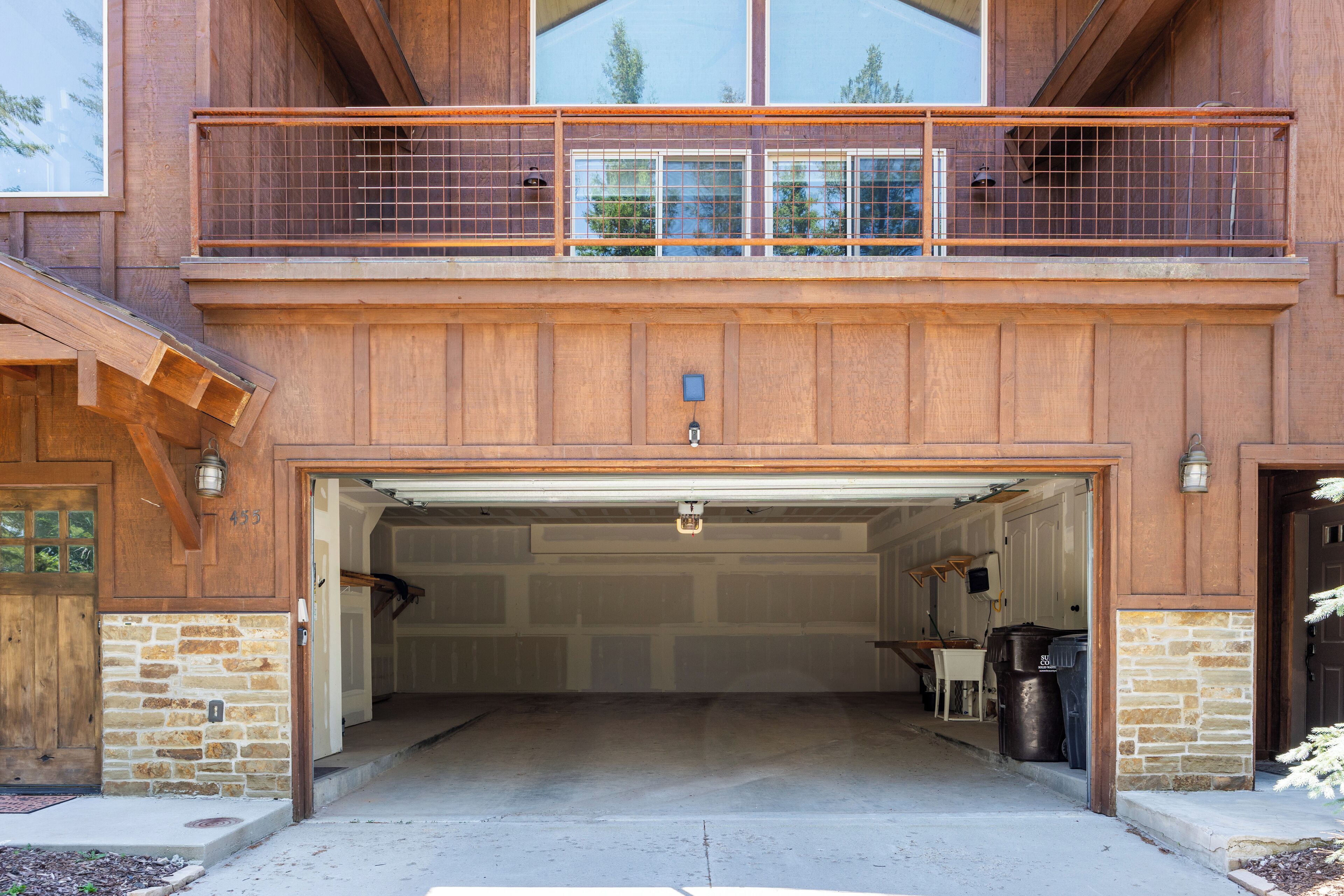 A two-story house with a garage entrance, wooden exterior, and a balcony with a metal railing.