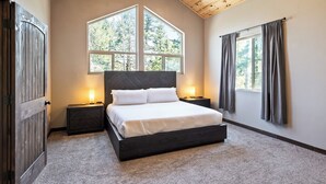 Ein Schlafzimmer mit einem großen Bett, zwei Nachttischen mit Lampen, einer Holzzahlung und einem Fenster mit Vorhängen.