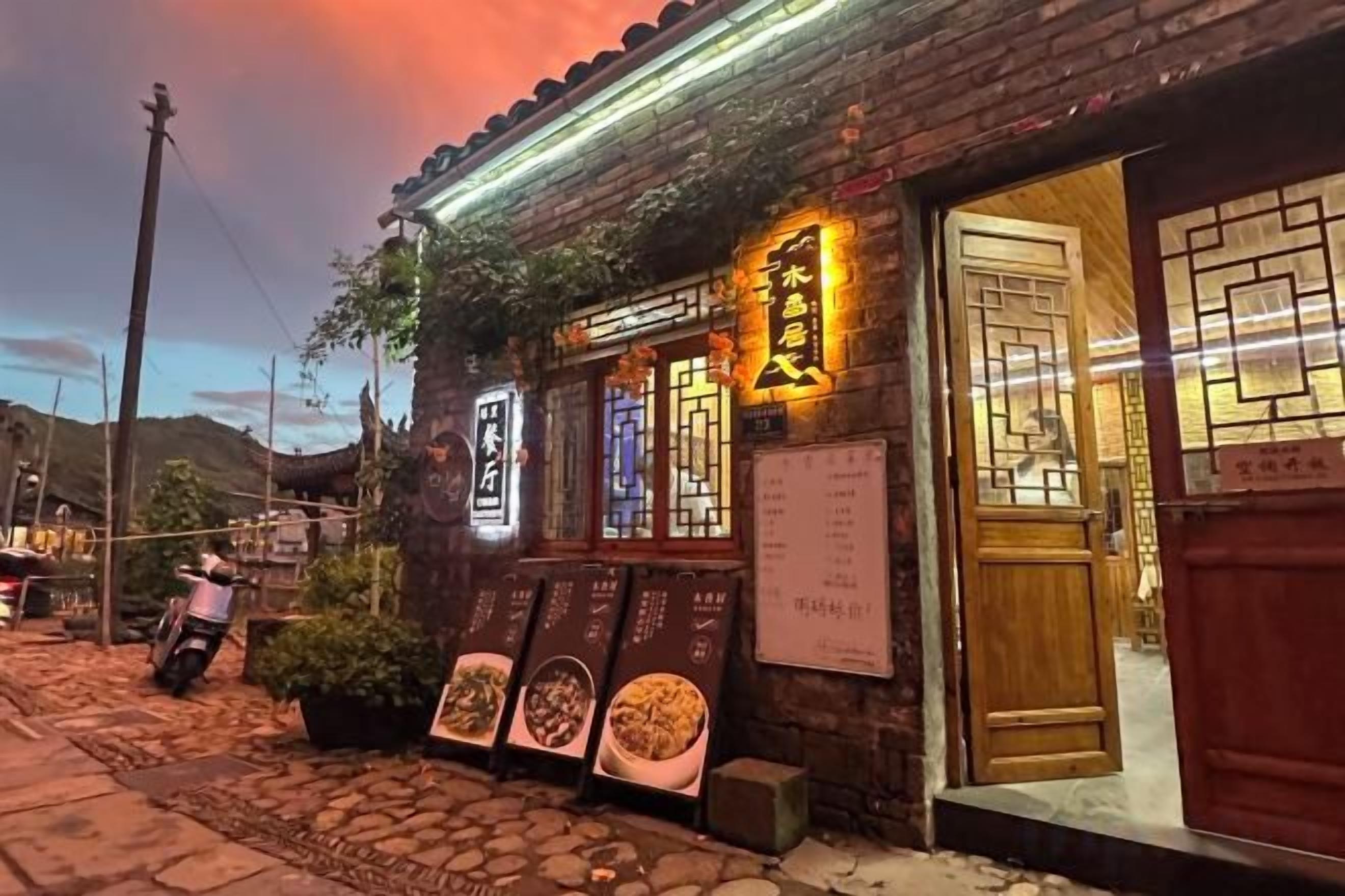 A traditional building with a wooden door and signage, a stone-paved entrance, and a menu board outside.