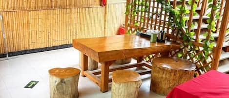 Una mesa de madera con taburetes, mantel rojo y pared de bambú.
