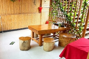 Una mesa de madera con taburetes, mantel rojo y pared de bambú.