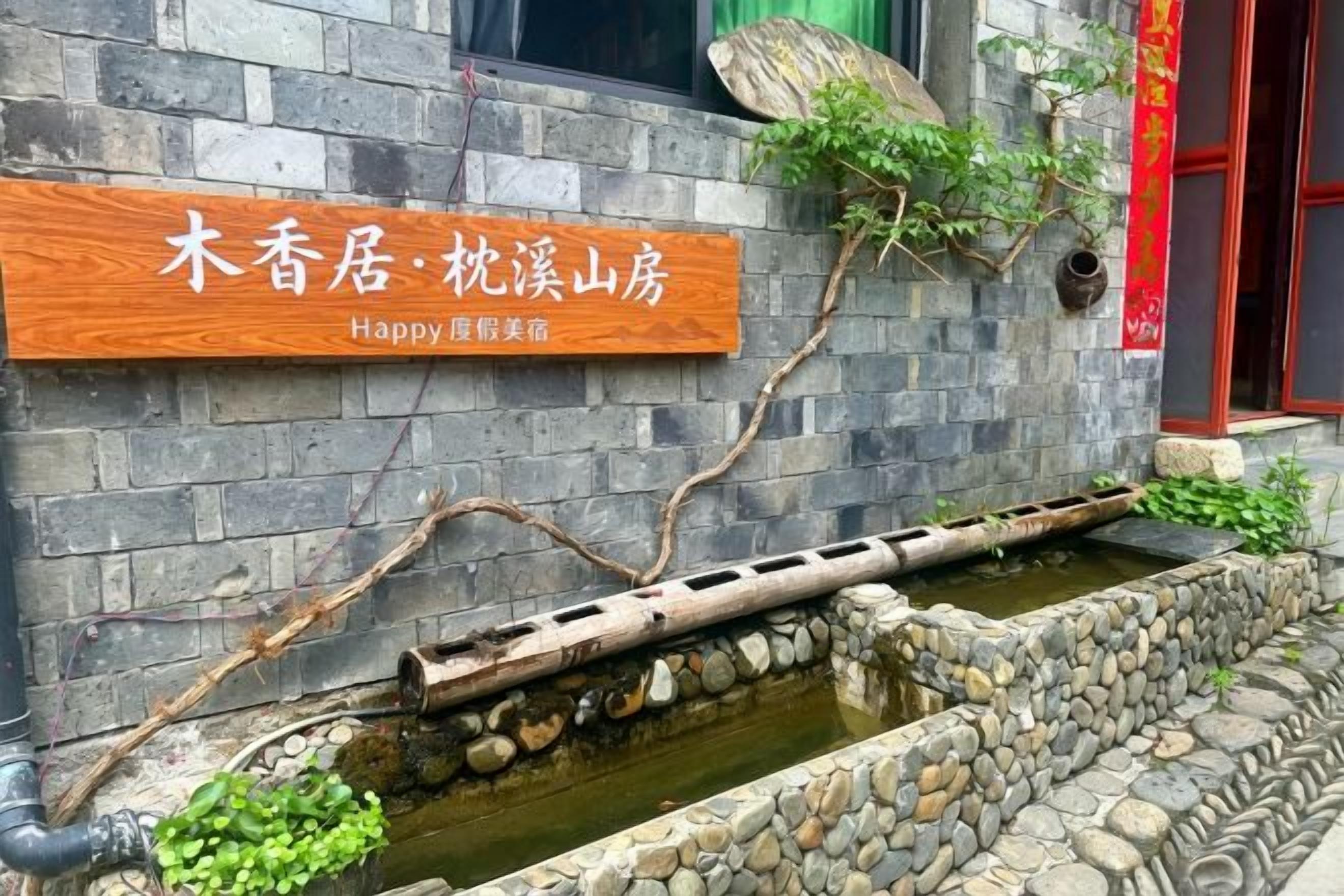 A stone wall with a wooden sign, a small water feature, and a red door.