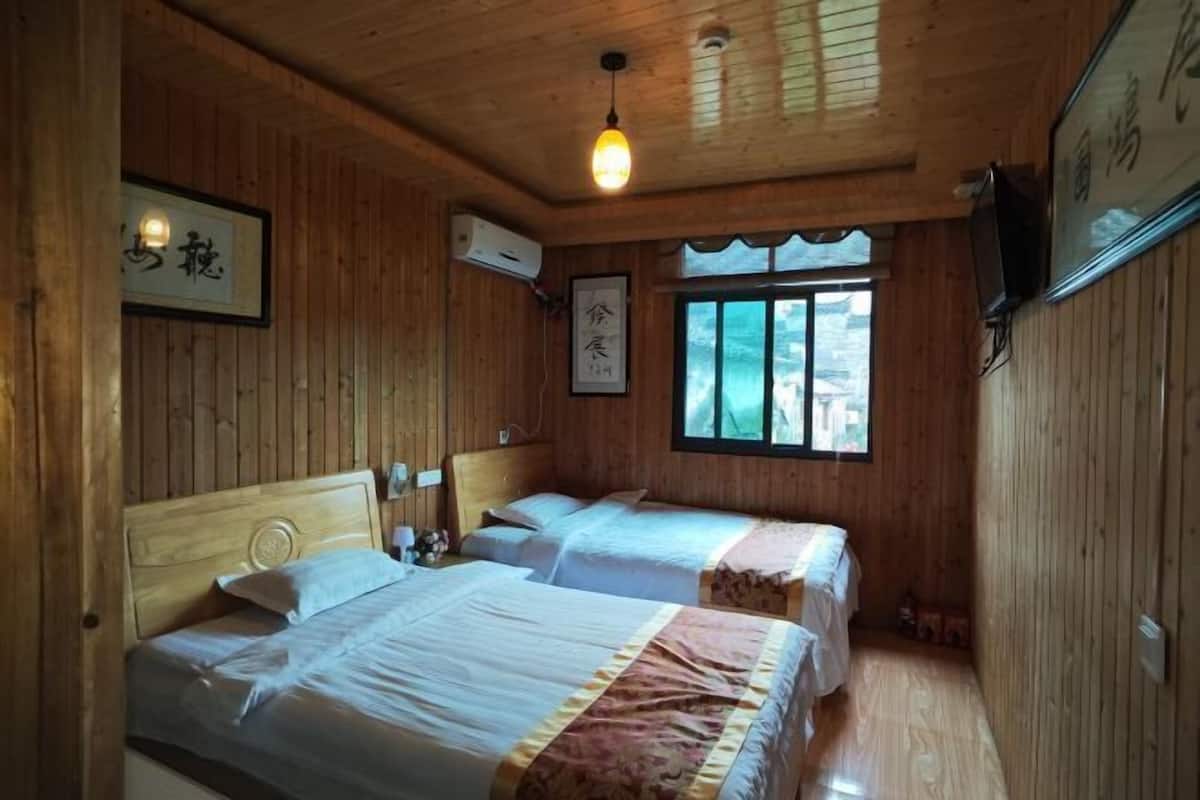 A wooden cabin room with two beds, a window, and a mounted television.
