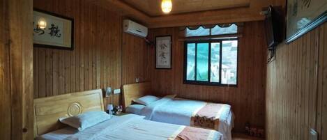 A wooden cabin room with two beds, a window, and a mounted television.
