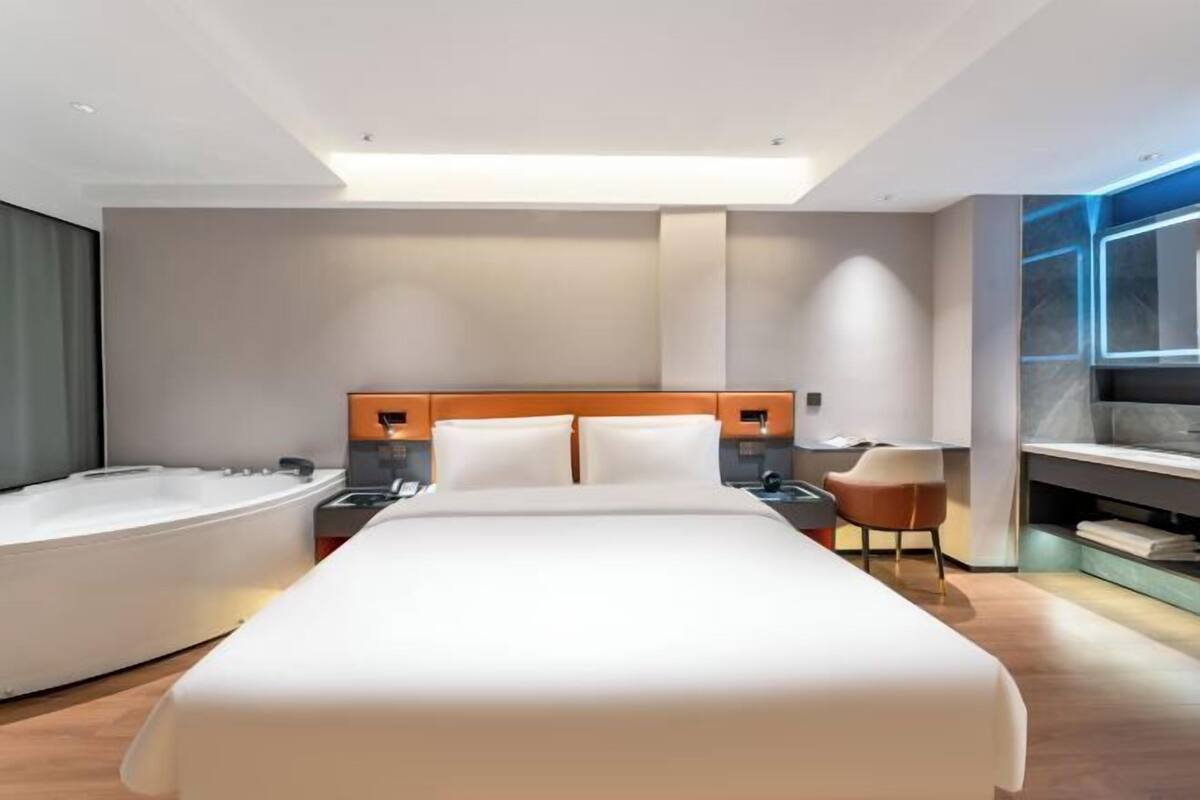 Habitación de hotel moderna con una cama grande, un baño separado con bañera, un escritorio y una silla.