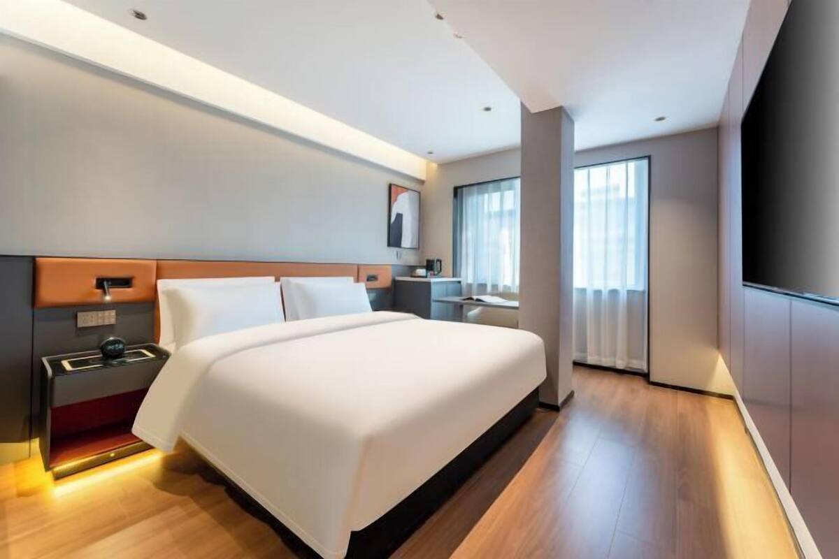 Habitación de hotel moderna con una cama grande, mesitas de noche, un escritorio y un ventanal con cortinas.