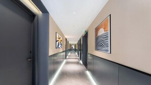 Egy modern hotel folyosó, hosszú, nyújtott kialakítással, a falakon elhelyezett, keretezett műalkotásokkal és szőnyeggel borított padlóval.