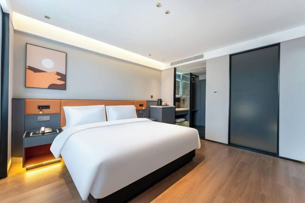 Una habitación de hotel moderna con una cama grande, mesitas de noche, un armario y un baño visible a través de una puerta abierta.