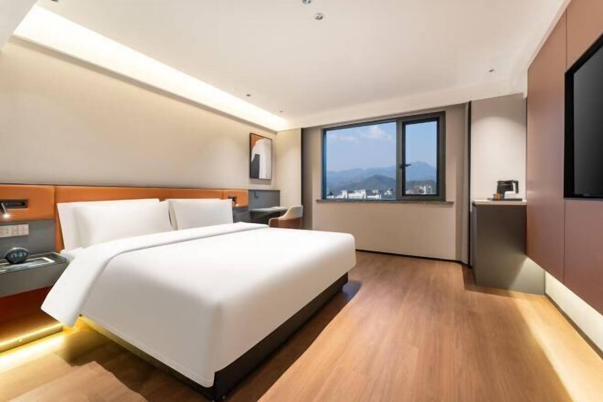 Una habitación de hotel moderna con una cama grande, un escritorio y un ventanal con vistas a la ciudad.