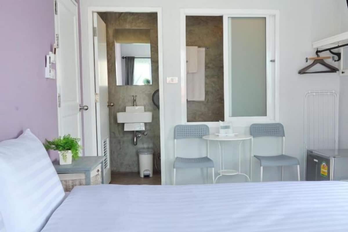 A bedroom with a bed, a small table with two chairs, a mirror, and a bathroom with a sink and towel rack.