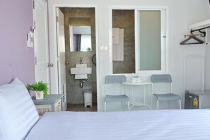 A bedroom with a bed, a small table with two chairs, a mirror, and a bathroom with a sink and towel rack. - Kata Bai D (Phuket)