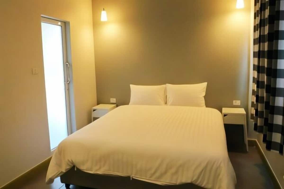 A hotel room with a bed, bedside tables, a door, and a curtain.