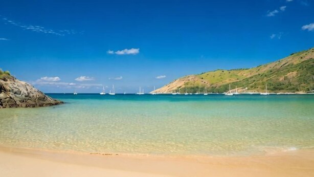 Une plage avec une eau cristalline, des bateaux et des collines.