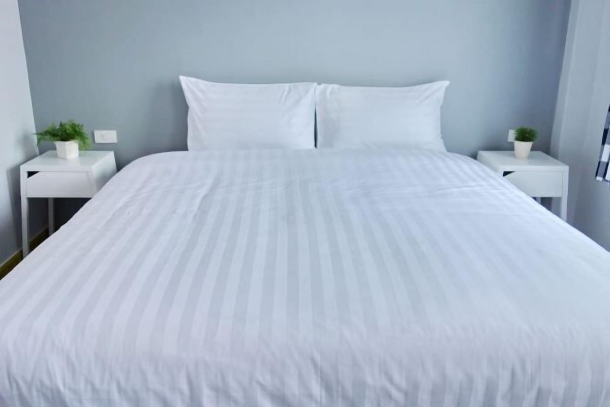 A bed with white bedding, two white nightstands with small potted plants, and a light blue wall.