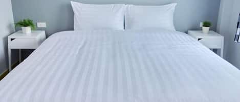 A bed with white bedding, two white nightstands with small potted plants, and a light blue wall.