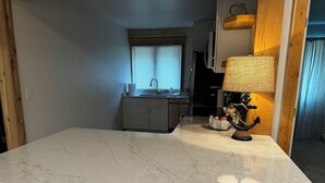 Une cuisine dotée d’un plan de travail en marbre, d’un petit îlot central, d’un évier et d’une lampe décorative.