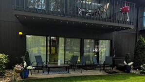 Un espace extérieur moderne aménagé avec des sièges, un mur en verre, une petite table et des chaises.