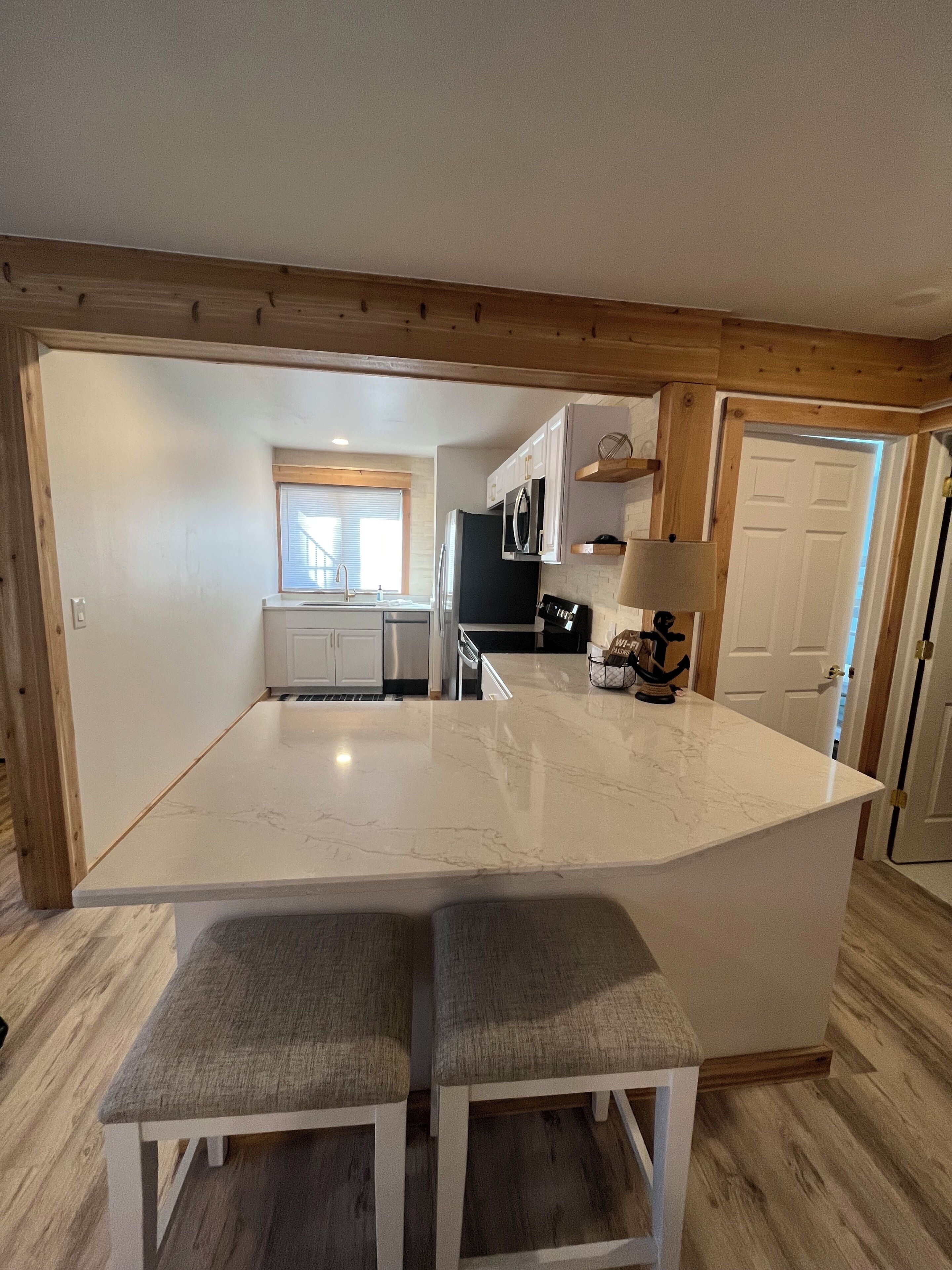 A kitchen with a central island, wooden beams, white cabinets, and a window with blinds.