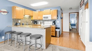 A kitchen with wooden cabinets, a white microwave, a brick backsplash, and a bar stool area. - Golden Reef! NEW pool! State park views! GR102 (Osage Beach)