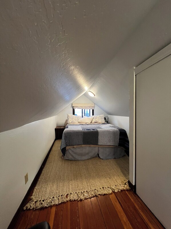 A small, sloped-roofed attic bedroom with a single bed, a large woven rug, and a ceiling light. - Cozy quiet & relaxing hide-a-way in the heart of Sausalito's ‘Hurricane Gulch.’ (Sausalito)