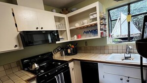 A kitchen with white cabinets, a black stove, a microwave, and a window with a sailboat view. - Cozy quiet & relaxing hide-a-way in the heart of Sausalito's ‘Hurricane Gulch.’ (Sausalito)