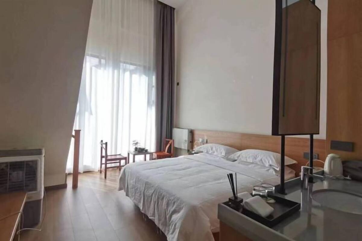 A hotel room with a bed, bedside table, chair, and a window with curtains.