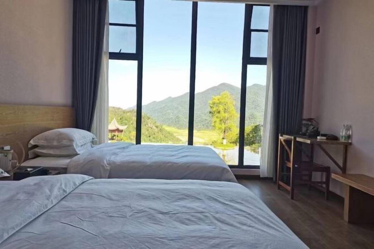 A hotel room with two beds, a desk, and a view of mountains.