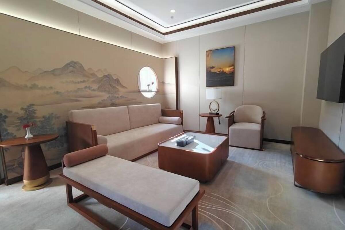 A modern living room with a sofa, a coffee table, a chair, and a TV. There is a painting on the wall and a round mirror.