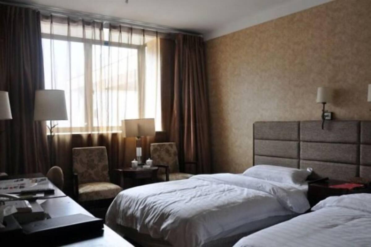 A hotel room with two beds, a desk, a chair, and a window with curtains.