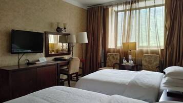 A hotel room with two beds, a desk with a TV, a chair, and a window with curtains.