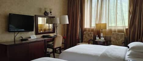 A hotel room with two beds, a desk with a TV, a chair, and a window with curtains.