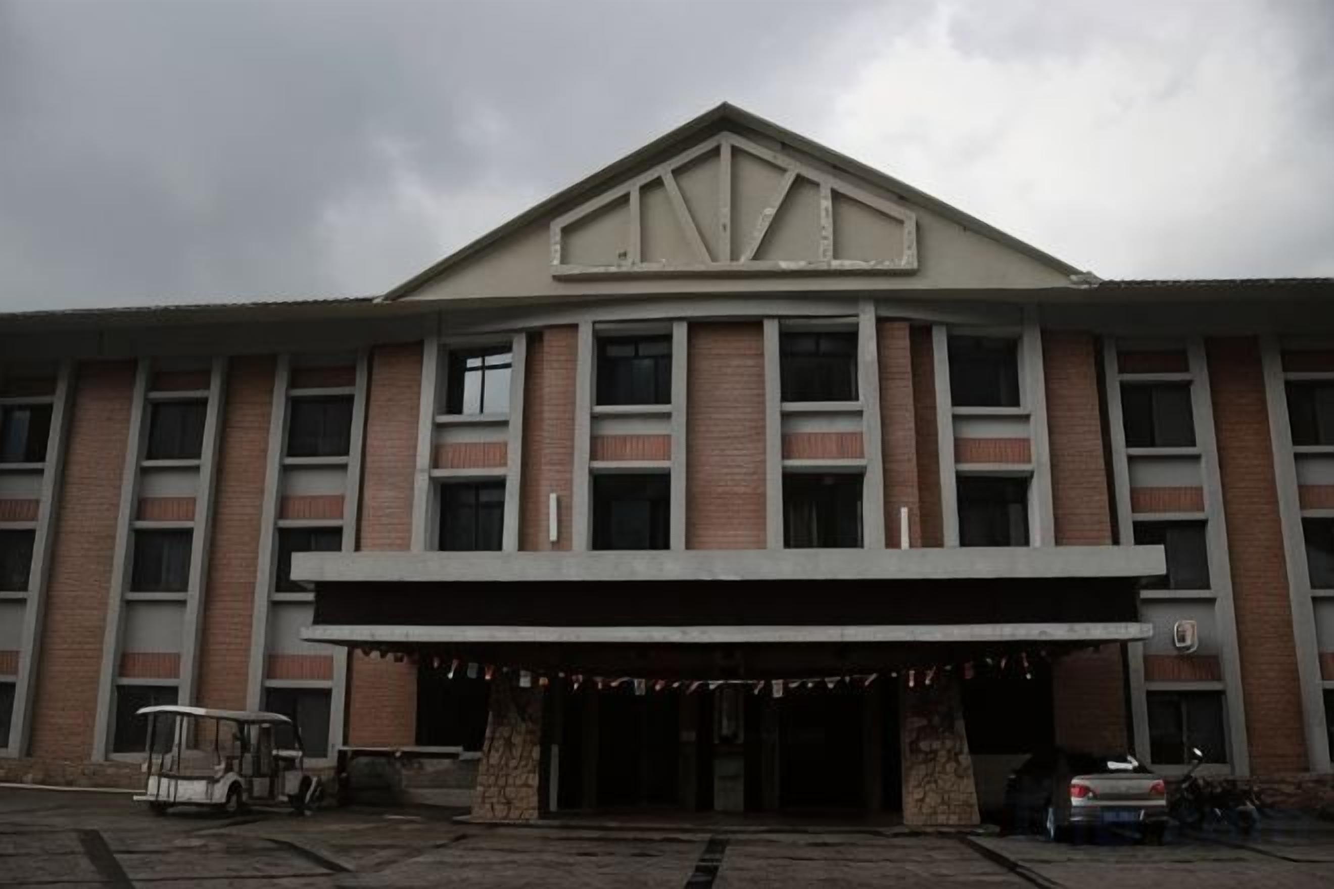 A building with a central entrance, multiple windows, and a parking area with a vehicle and a golf cart.