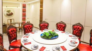 A round dining table with red upholstered chairs, a central floral arrangement, and neatly arranged place settings.
