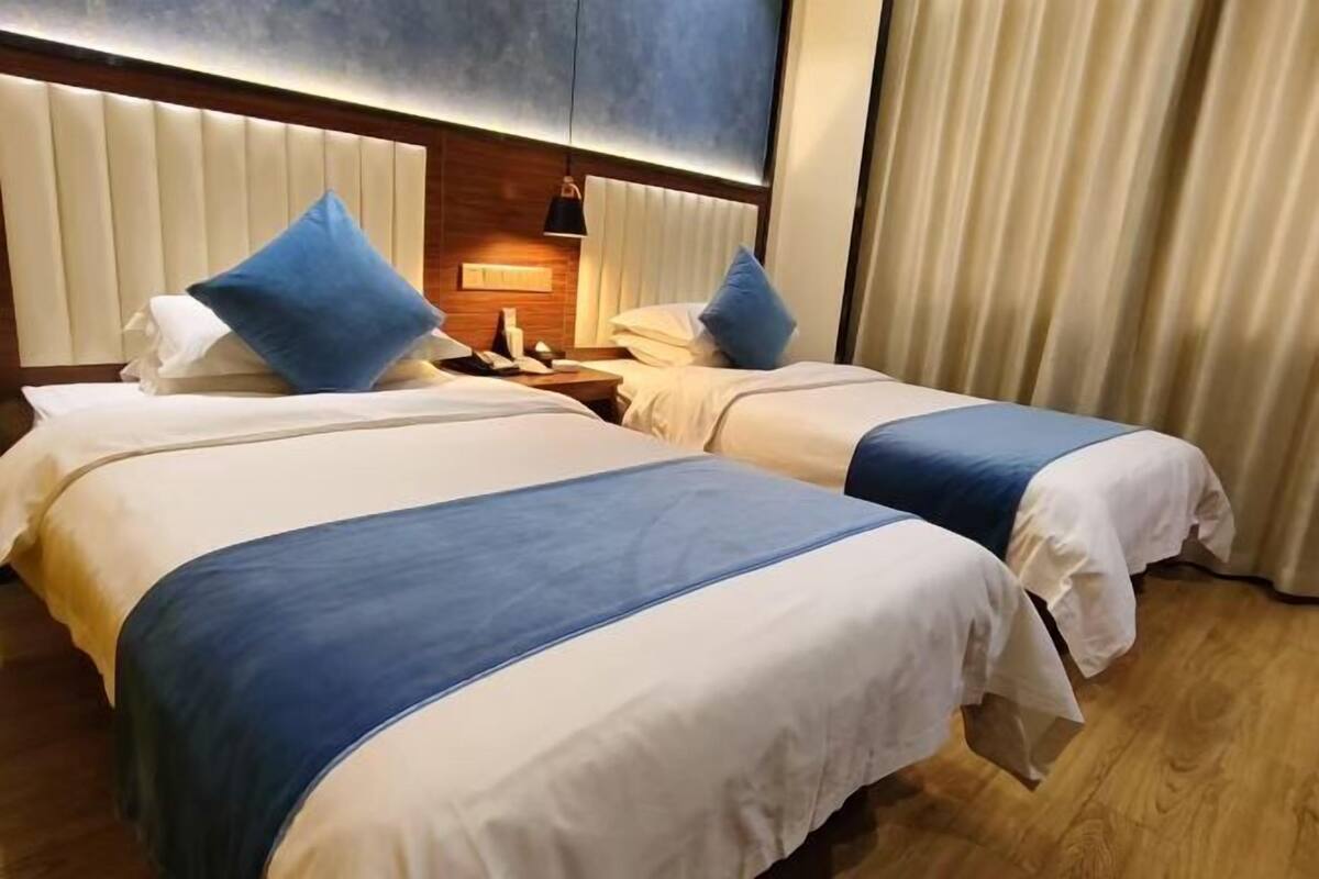 Une chambre d’hôtel avec deux lits, une tête de lit en bois, une table de chevet et une fenêtre avec des rideaux.