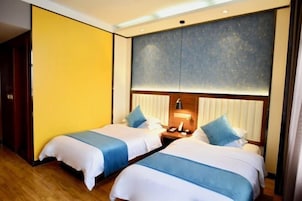 Habitación de hotel con dos camas, suelo de madera, una pared grande con diseño texturizado y una mesita de noche con lámpara.