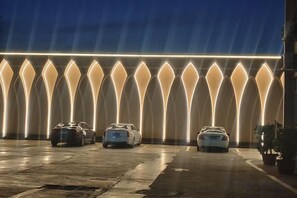 A parking area with cars and a modern illuminated wall structure.