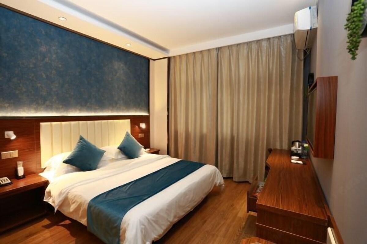 Une chambre d’hôtel avec un grand lit, un bureau en bois, un téléviseur fixé au mur et une grande fenêtre avec des rideaux.