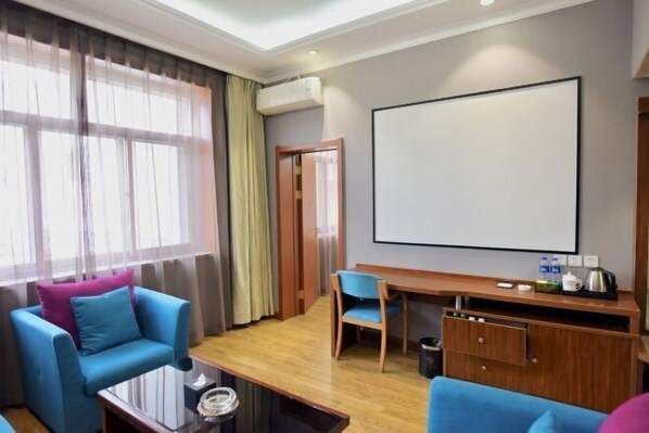Une chambre d’hôtel moderne dotée d’une grande fenêtre, d’un coin salon avec des canapés bleus, d’un bureau en bois et d’un grand écran.