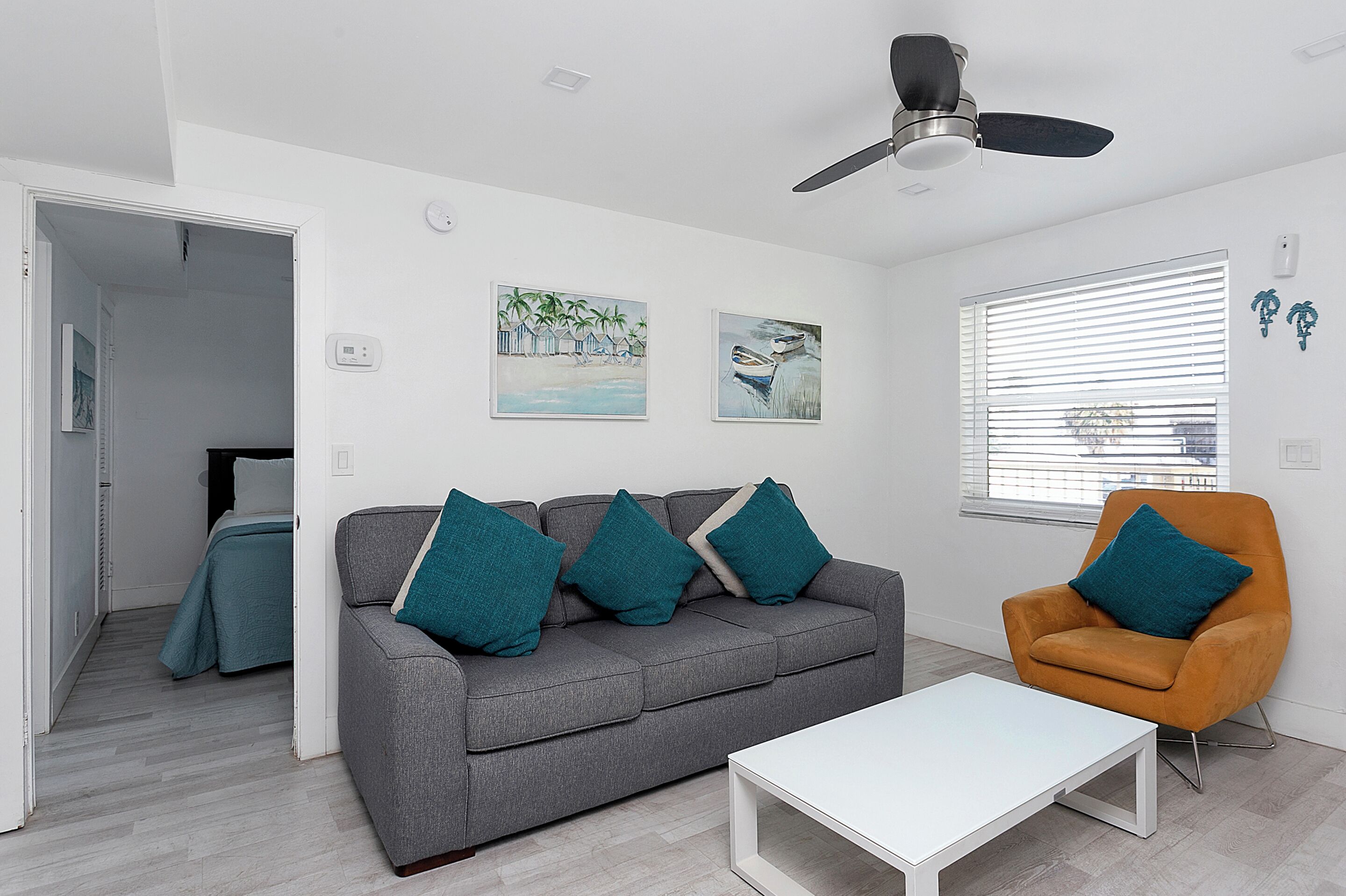 A modern living room with a grey sofa, teal cushions, a white coffee table, and a ceiling fan.