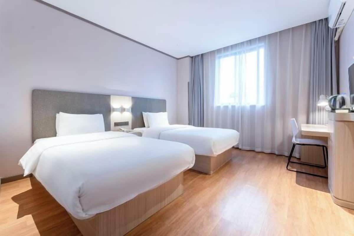 A hotel room with two beds, a desk, a chair, and a window with curtains.