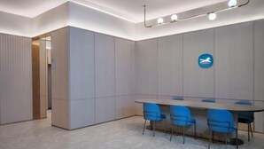 A modern conference room with a long table and blue chairs, a ceiling light fixture, and a logo on the wall. - HanTing Hotel (Ganzhou Jiangnan Songcheng Wenming Avenue) (Ganzhou)