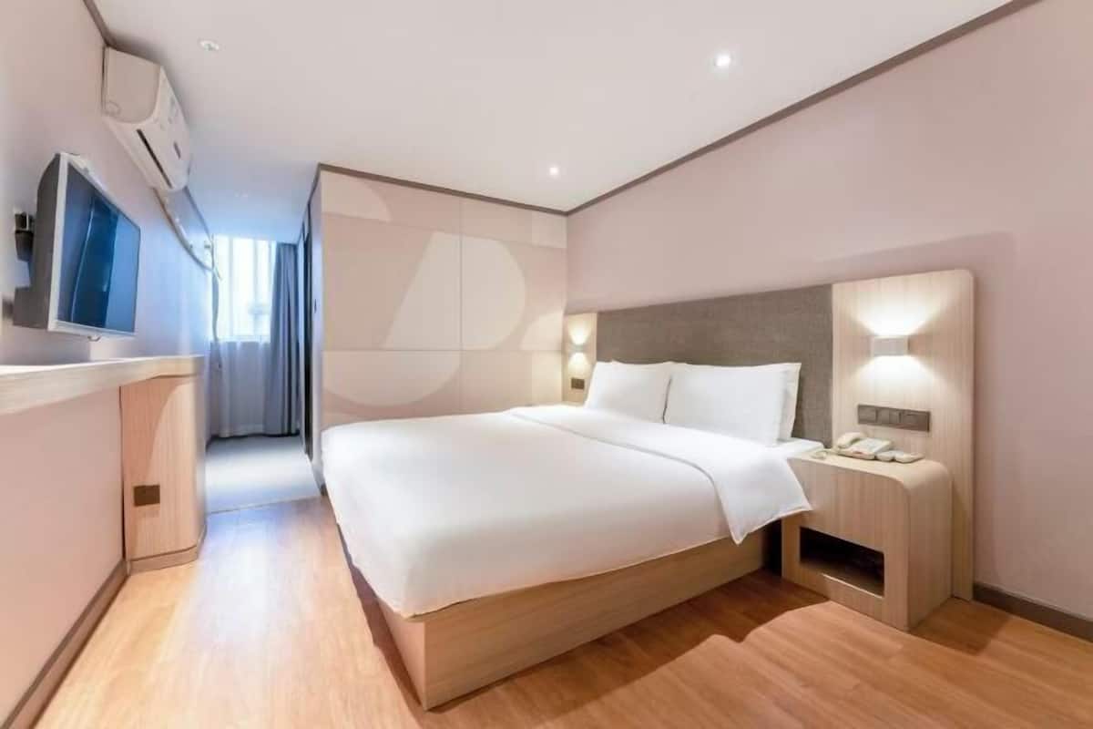 A modern hotel room with a large bed, bedside tables, a TV, and an air conditioning unit.