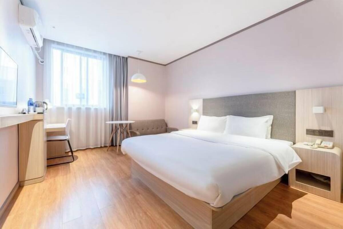 A modern hotel room with a large bed, a desk, a chair, and a small table.