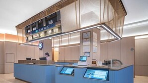 A reception area with a blue counter, digital displays, and a suspended ceiling with a mesh design. - HanTing Hotel (Ganzhou Jiangnan Songcheng Wenming Avenue) (Ganzhou)
