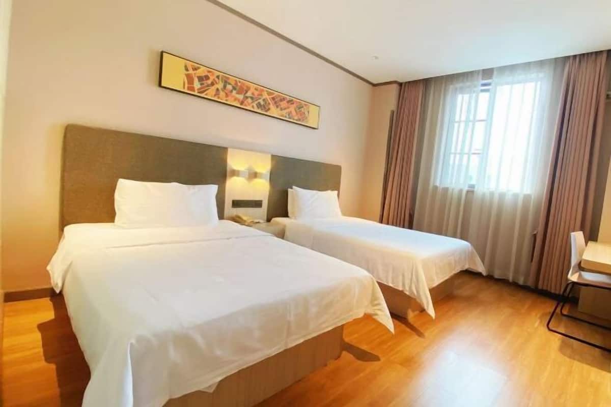A hotel room with two beds, a desk, and a large window with curtains.