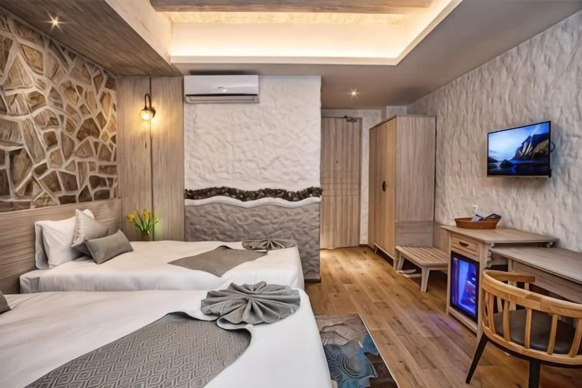 Une chambre d’hôtel moderne avec un mur en pierre, un téléviseur à écran plat, un lit recouvert d’une courtepointe à motifs et une petite table en bois.