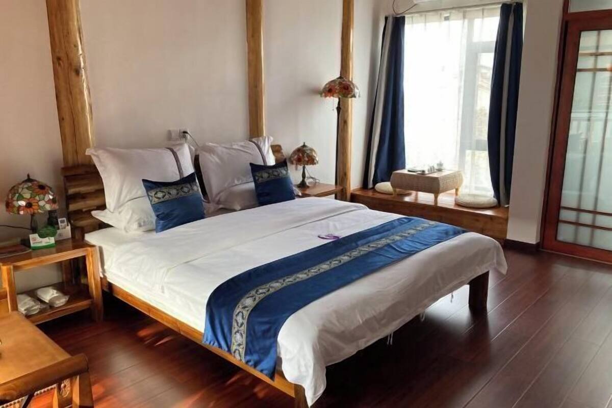 A bedroom with a wooden bed, white bedding, and a blue accent. There is a nightstand with a lamp, a small table with a globe, and a window with curtains.