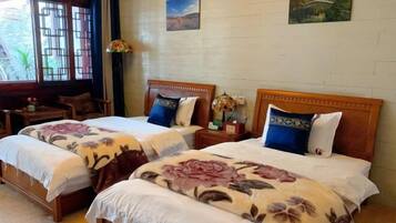 A hotel room with two beds, wooden headboards, floral bedspreads, a small table, and a window with a view of greenery.