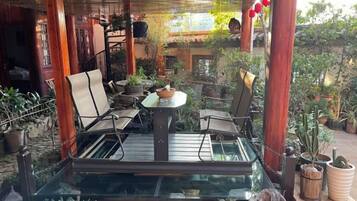 An outdoor patio with a glass table surrounded by chairs, potted plants, and wooden pillars.